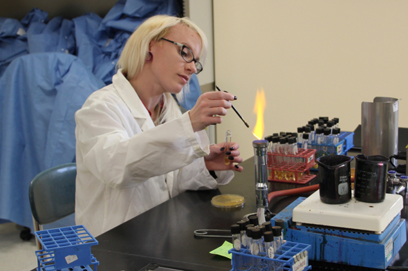 stem student in lab holding pipet and burning sample in bunsen burner