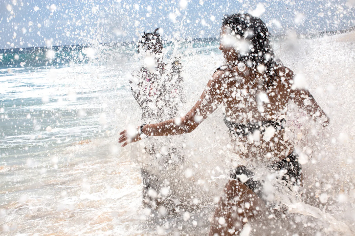 two women splashing white ocean foam as they run into the ocean