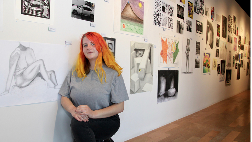student posing in front of art work at student artwork exhibit
