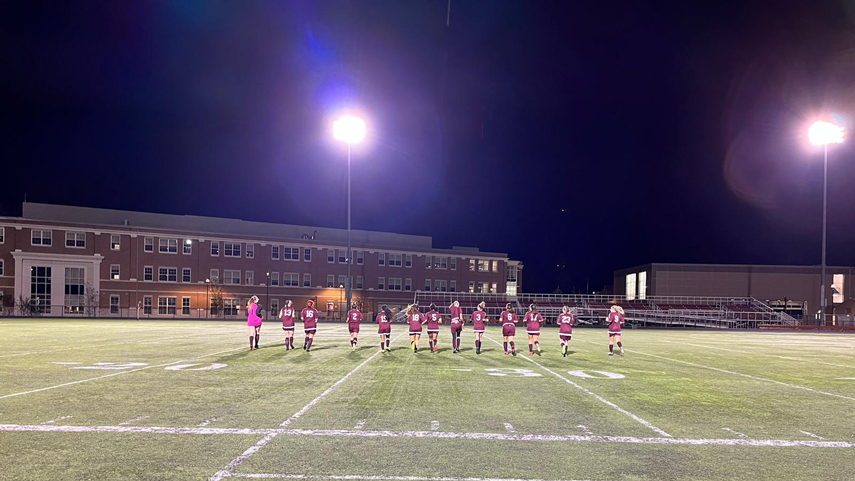 women's soccer team running out into field lit up by lights at night
