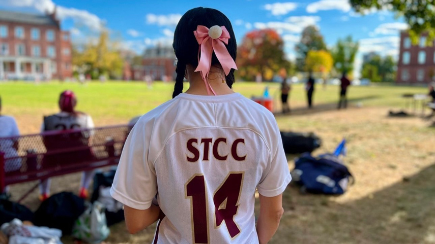 women's soccer player looking off at game with pink ribbbon in her hair in braids