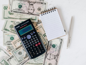 a calculator and notepad sitting on a pile of cash
