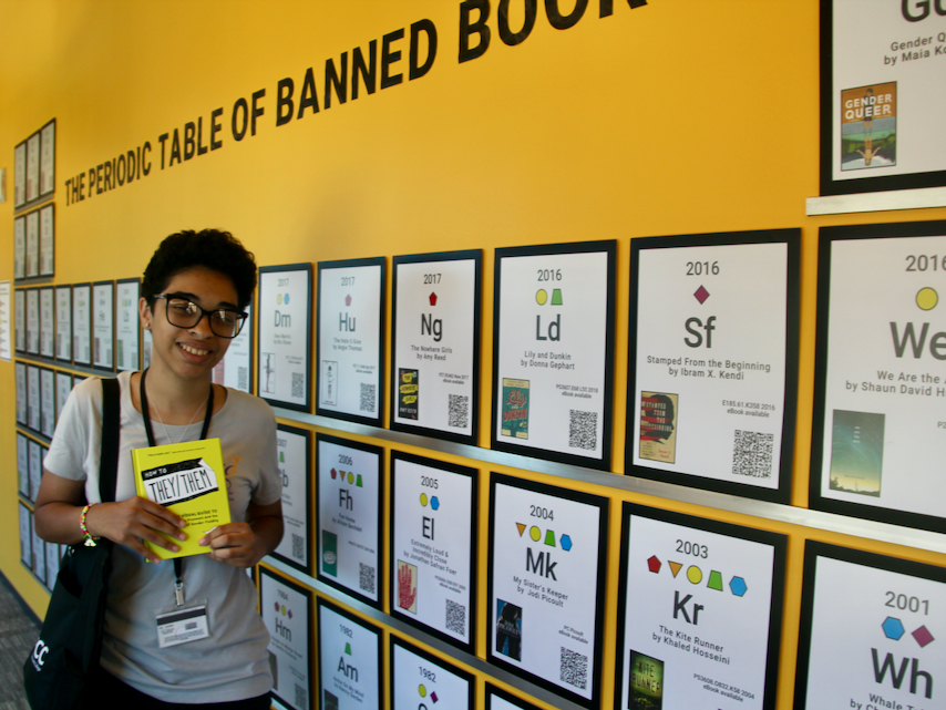 Student stands next to Banned Books exhibit in library