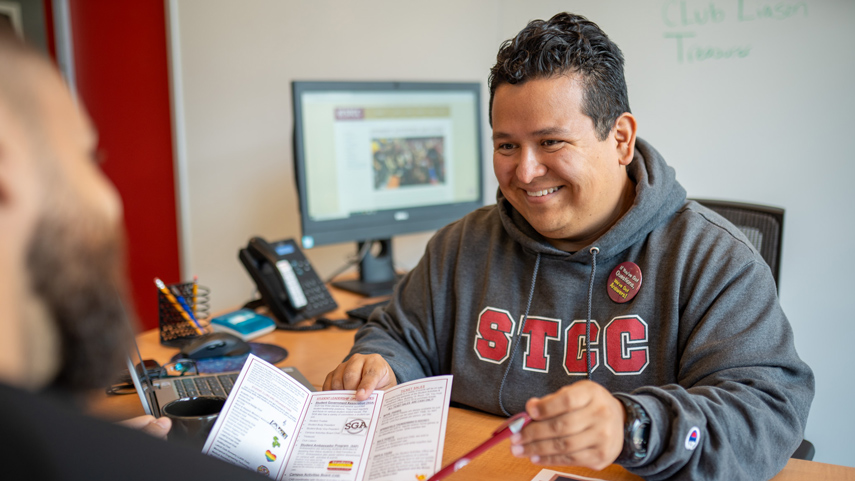 career advisor at desk with student pointing to brochure with pen