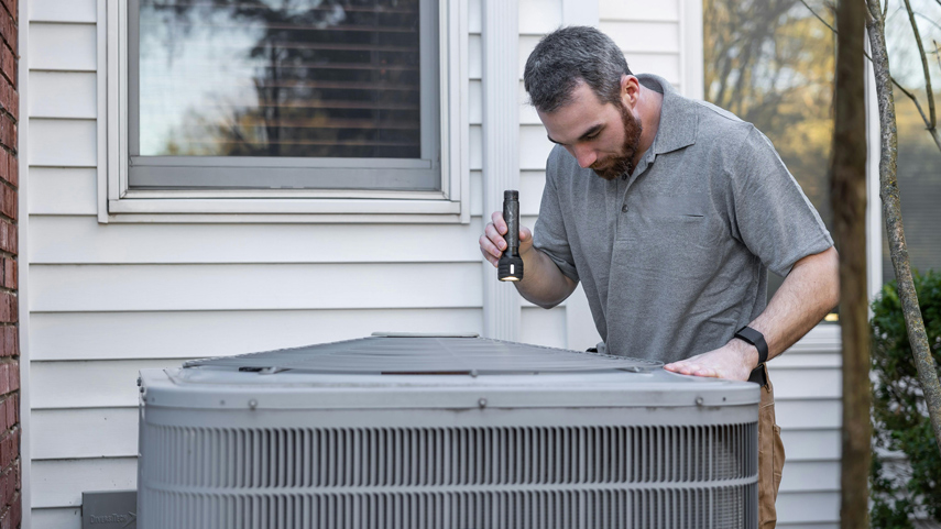 HVAC technician pointing flashlight at cooling unit
