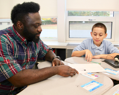 Para Educator at table helping elementary student